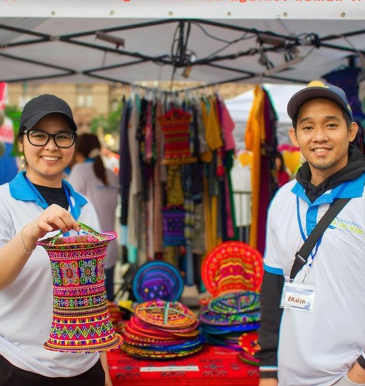 Two young adults smiling at their craft stall at an outdoor market (stock photo)